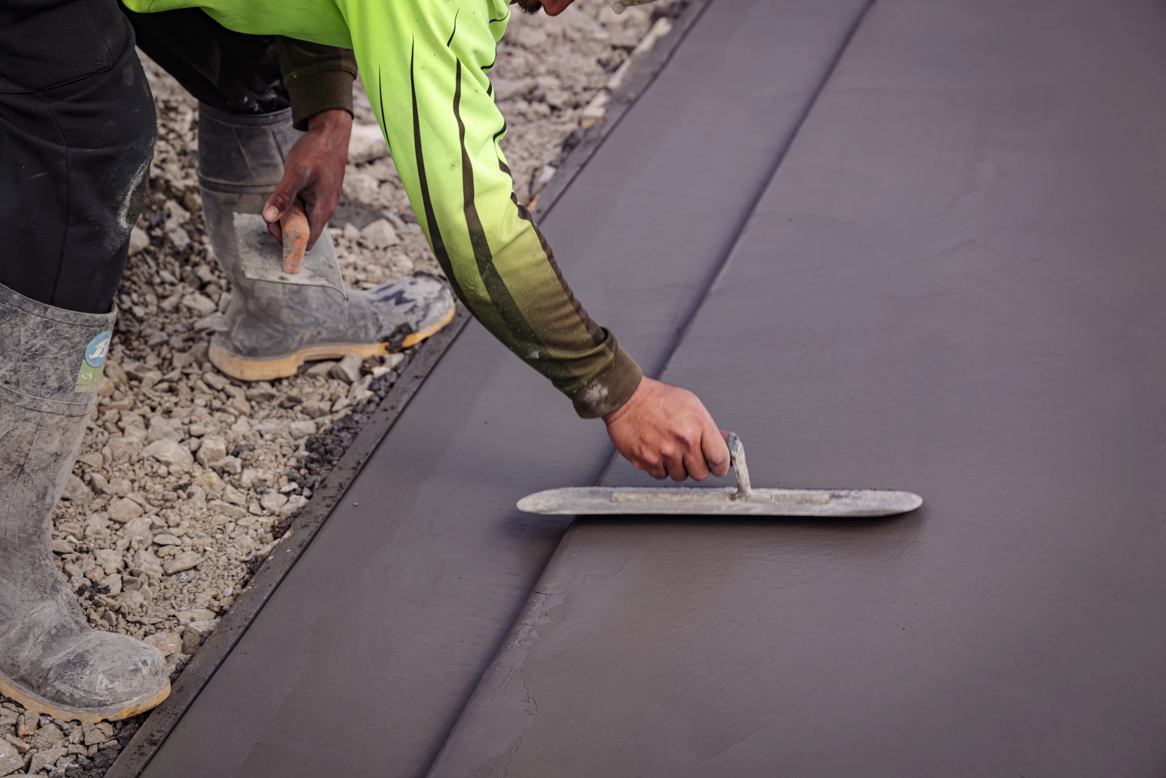 Livic Civil concreter trowelling a dark concrete slab beside the prepared base.