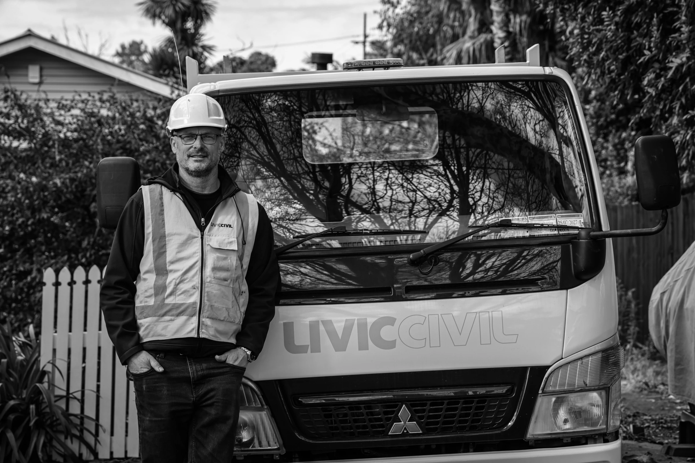 Livic Civil team member standing beside a Livic truck on a residential street in monochrome.