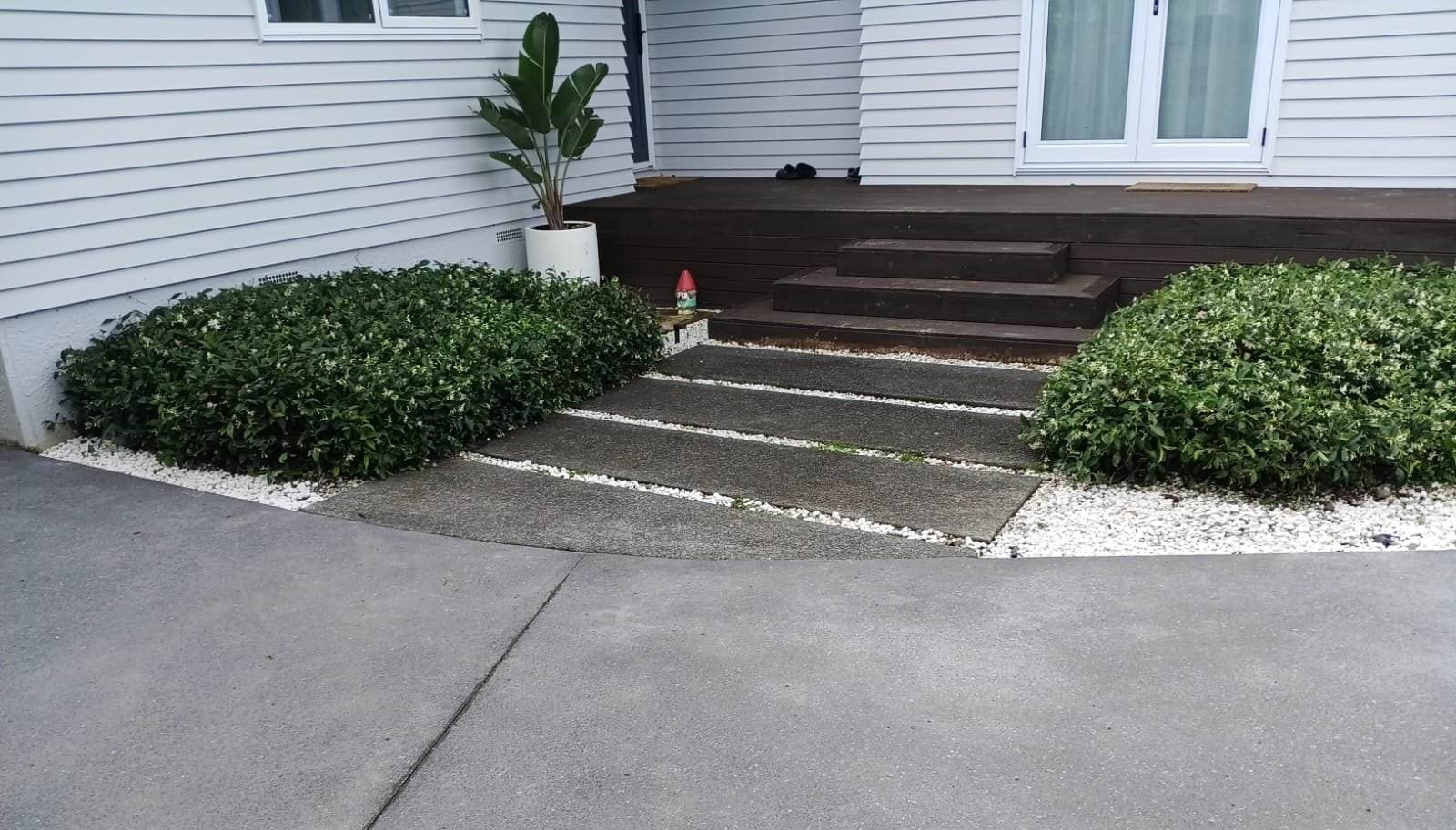 Concrete driveway and path beside the house, with planting and steps.