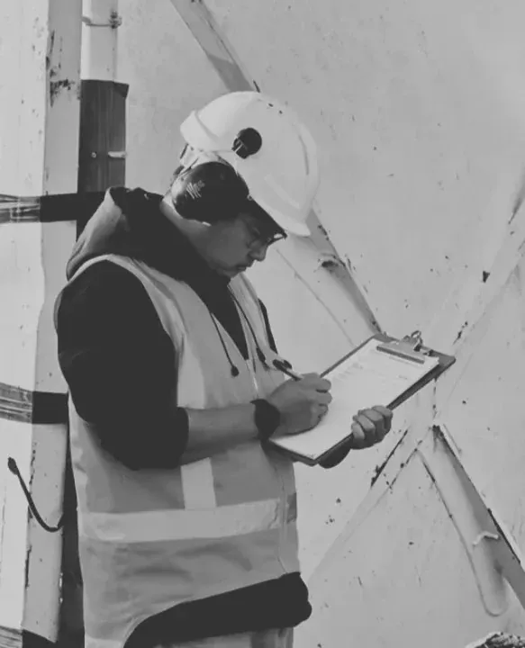 Site worker in a hard hat and high-visibility vest recording an inspection beside a concrete structure.