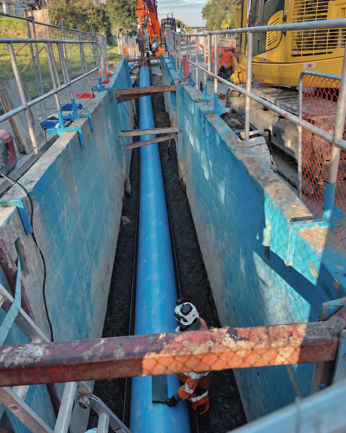 Blue watermain installed in a shored trench, with an excavator beside it.