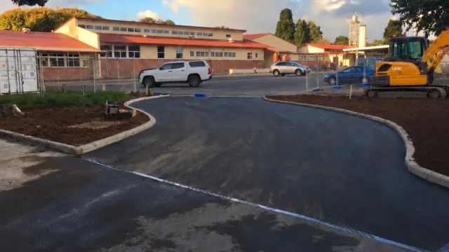 Curved asphalt accessway with concrete kerbs, temporary fencing and construction equipment.