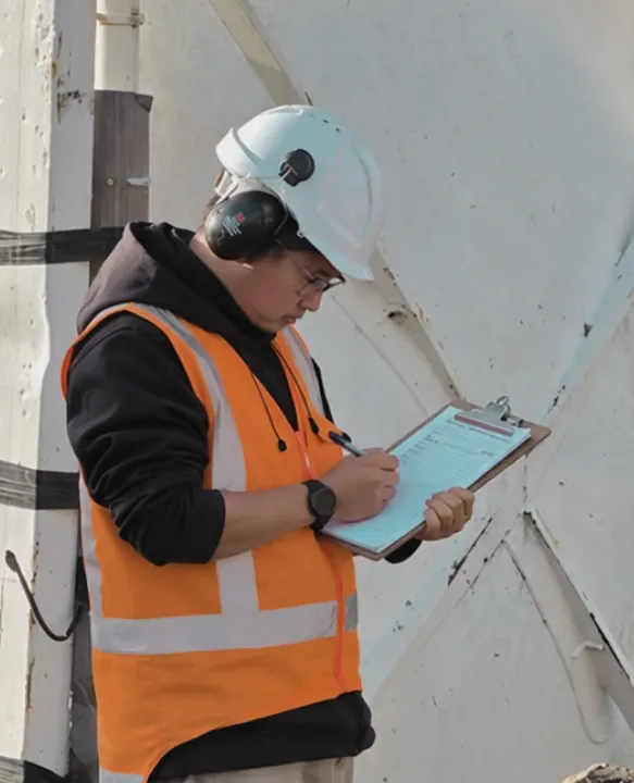 Site worker in a hard hat and high-visibility vest recording an inspection beside a concrete structure.