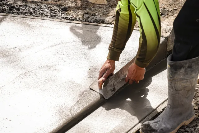 Concrete worker finishing a fresh slab with a hand trowel.