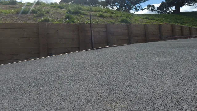 Textured concrete pavement beside a timber retaining wall and grassed slope.