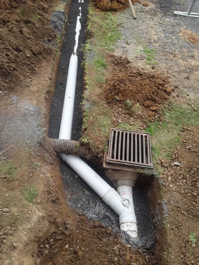 Stormwater drainage pipes and a catchpit being installed beside an excavated trench.
