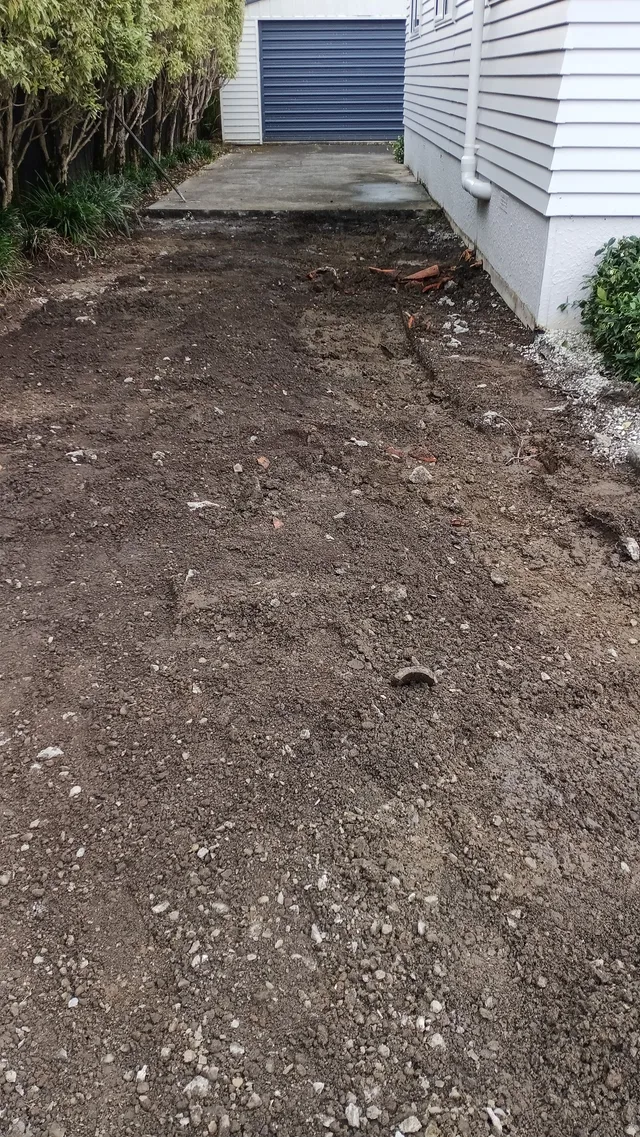 Excavated driveway base with material removed beside a house.